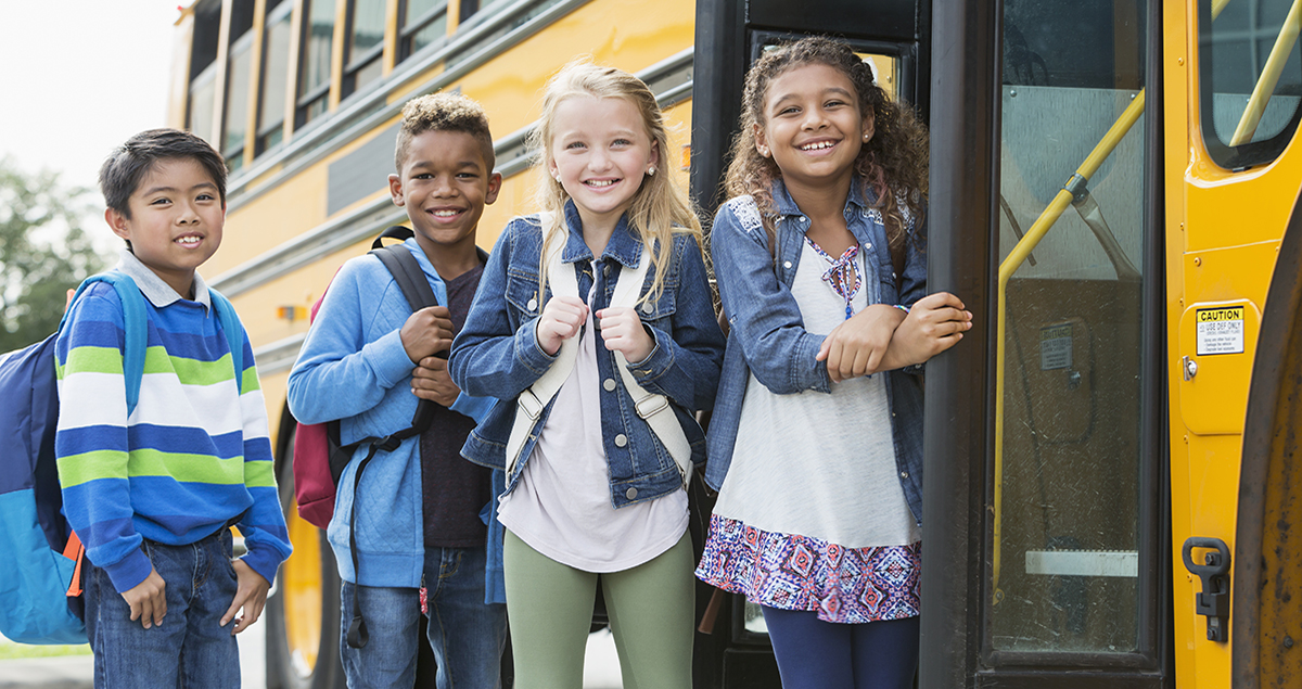 Multi-ethnic school children standing outside bus